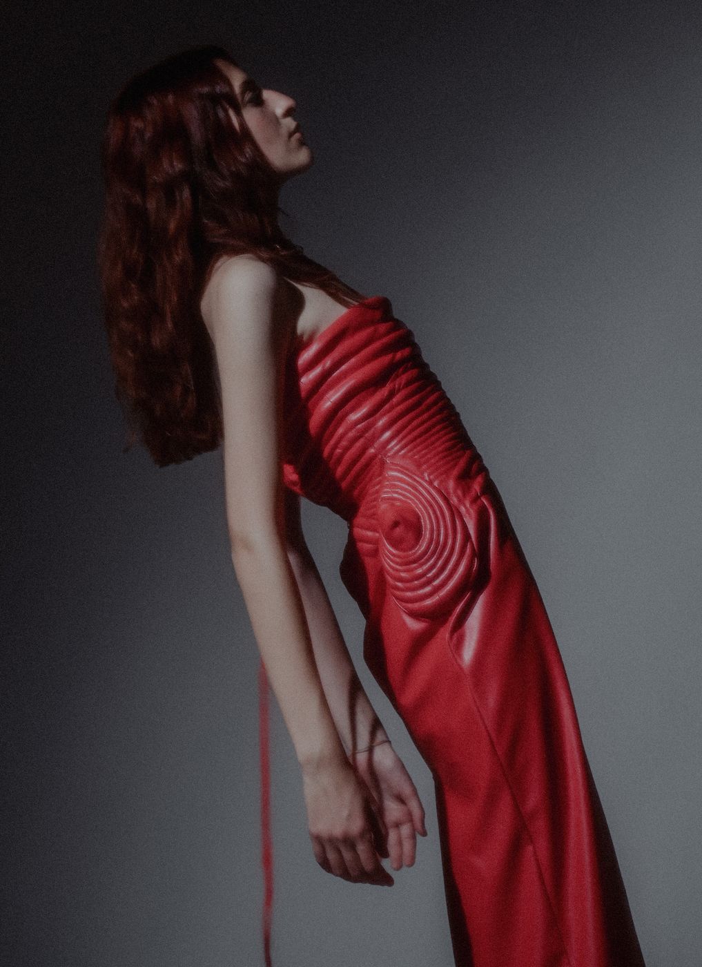 Model in a red draped dress from the DISTOPICA collection, crouching and looking into the camera