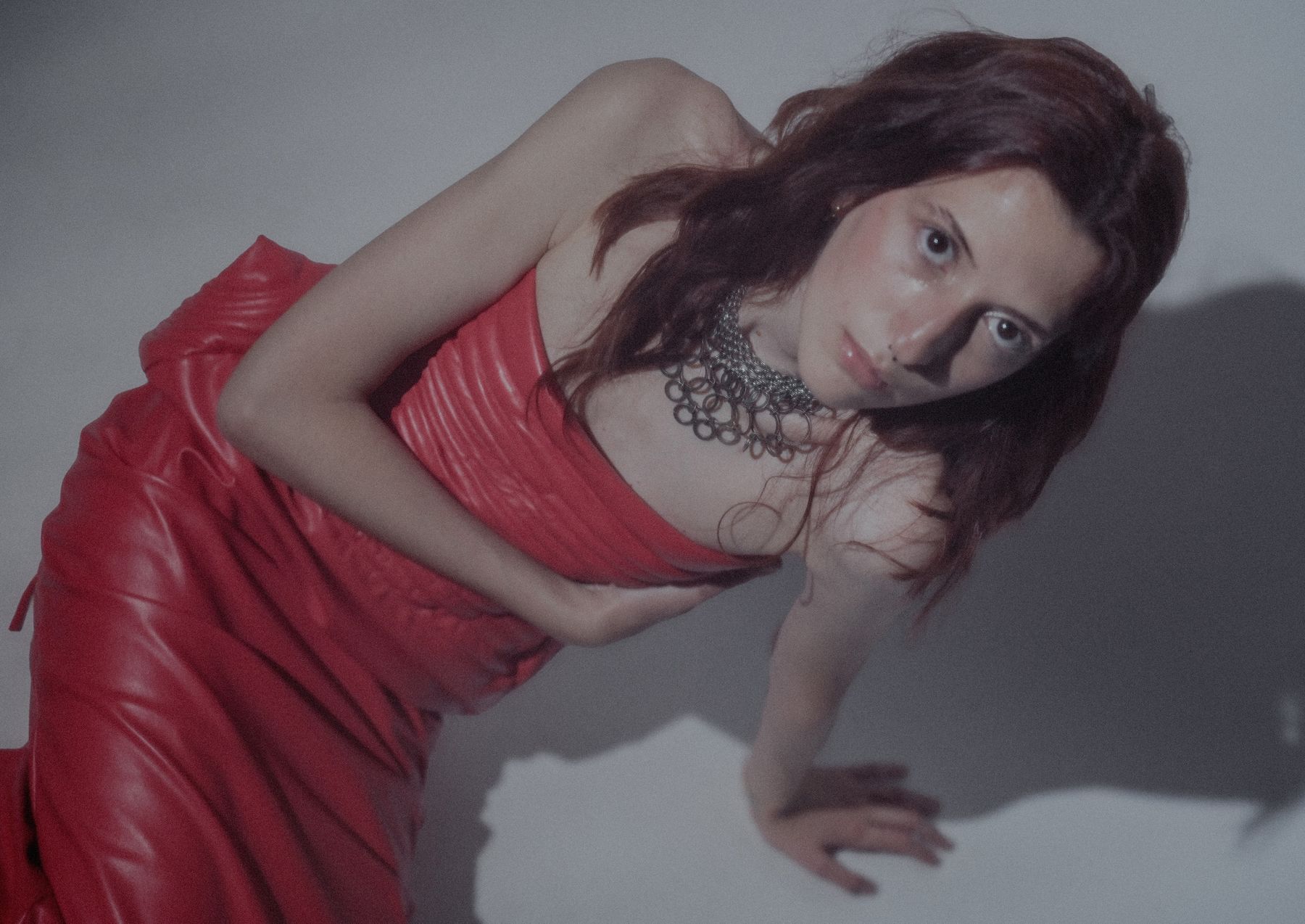 Model in red reclining on the floor, wearing a metal necklace