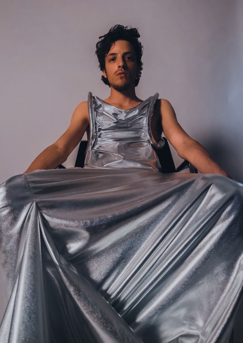 Male model seated, holding out a wide silver skirt